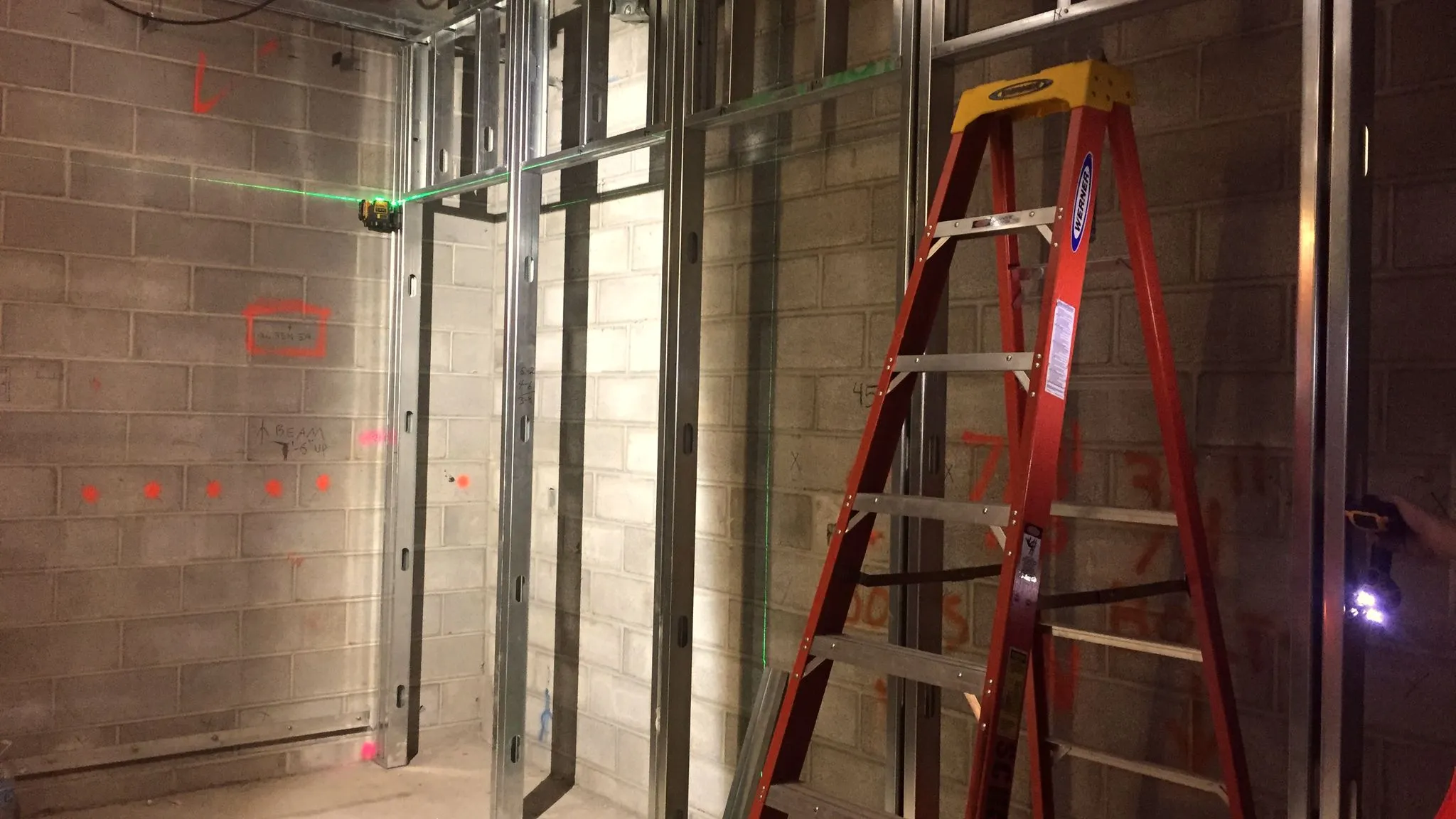 An office fit-out in progress: steel stud partitions with red setting-out marks, a green laser line and an orange stepladder.